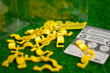 Yellow BudClips plant training clips by BudTrainer scattered on artificial grass with product instructions and packaging.