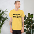 Man wearing a yellow BudTrainer t-shirt with 'I Grow Big Buds' text, standing in front of plants.